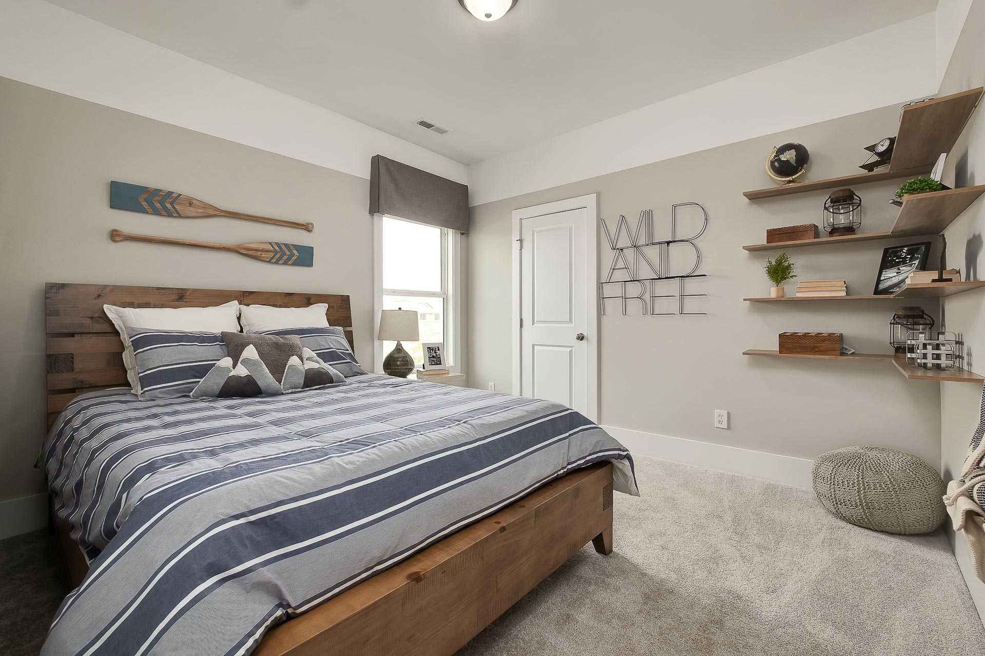 Cozy bedroom in The Everett by Davidson Homes featuring wooden bed with blue striped bedding, nautical oar decor, and wall shelves