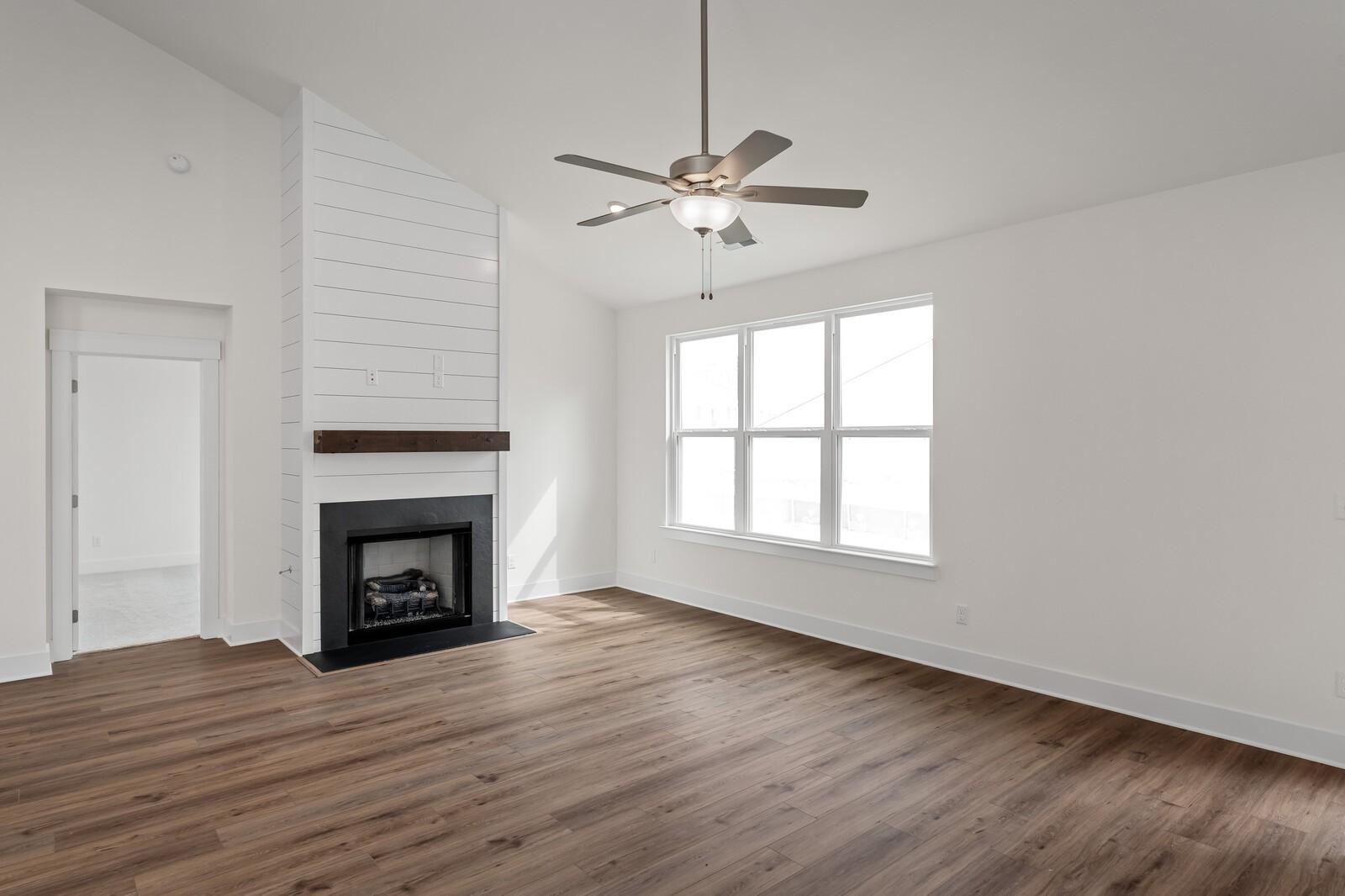 Cozy family room with shiplap gas fireplace, hardwood floors, ceiling fan, and large windows in Davidson Homes Ridgeport, Gallatin, Tennessee