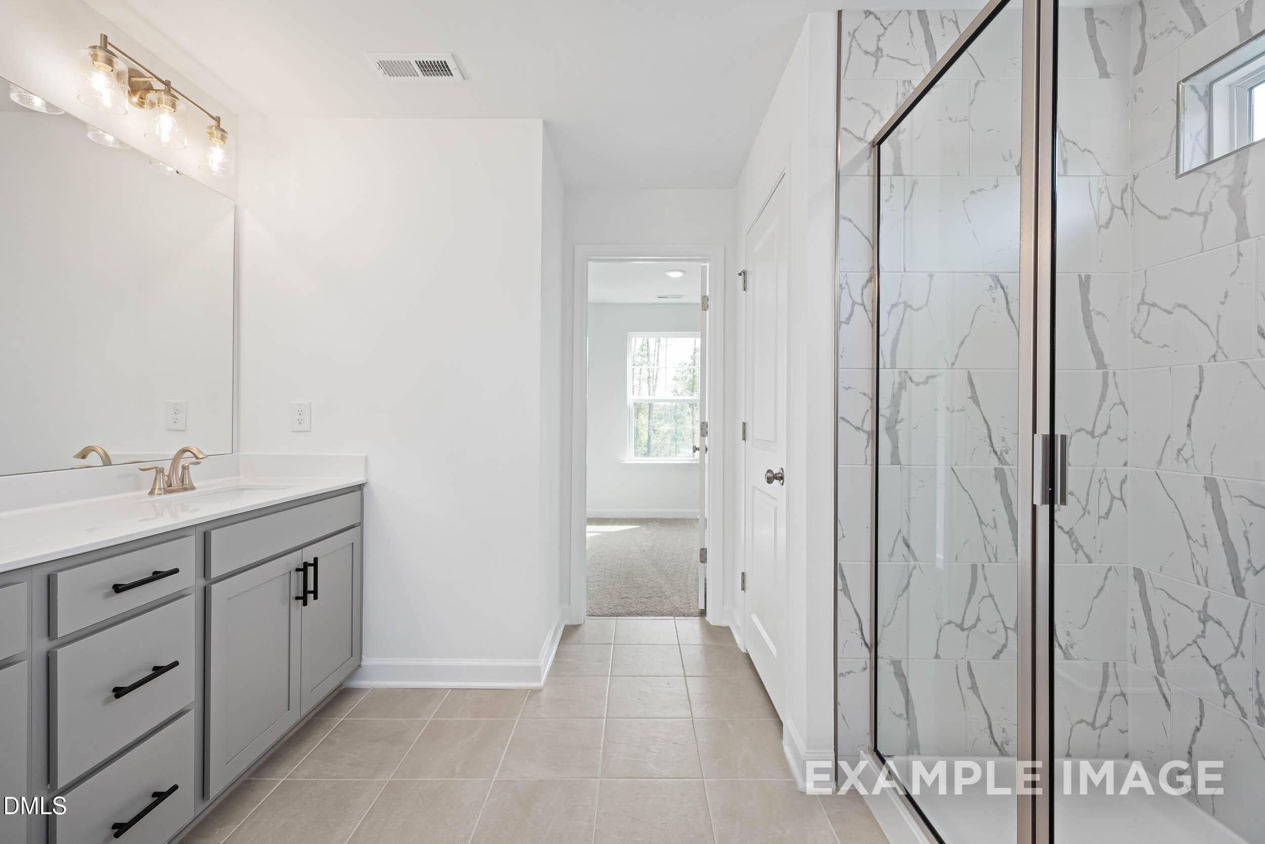 Elegant master bathroom with double gray vanity, frameless glass shower, white subway tile, gold fixtures in The Willow D, Zebulon, NC