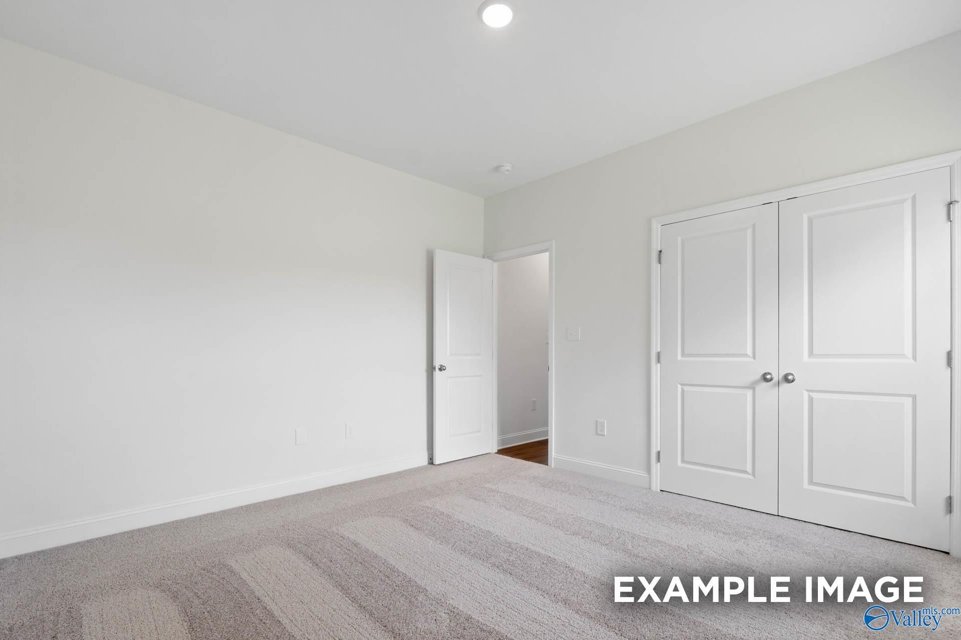 Spacious empty bedroom with light gray walls, double-door closet, and striped carpet in Davidson Homes The Oxford, Huntsville
