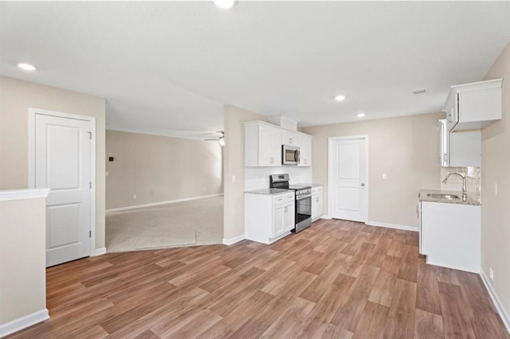 Modern open-concept kitchen with white cabinets, stainless steel appliances, and wood flooring in Davidson Homes The Washington, Phenix City, Alabama
