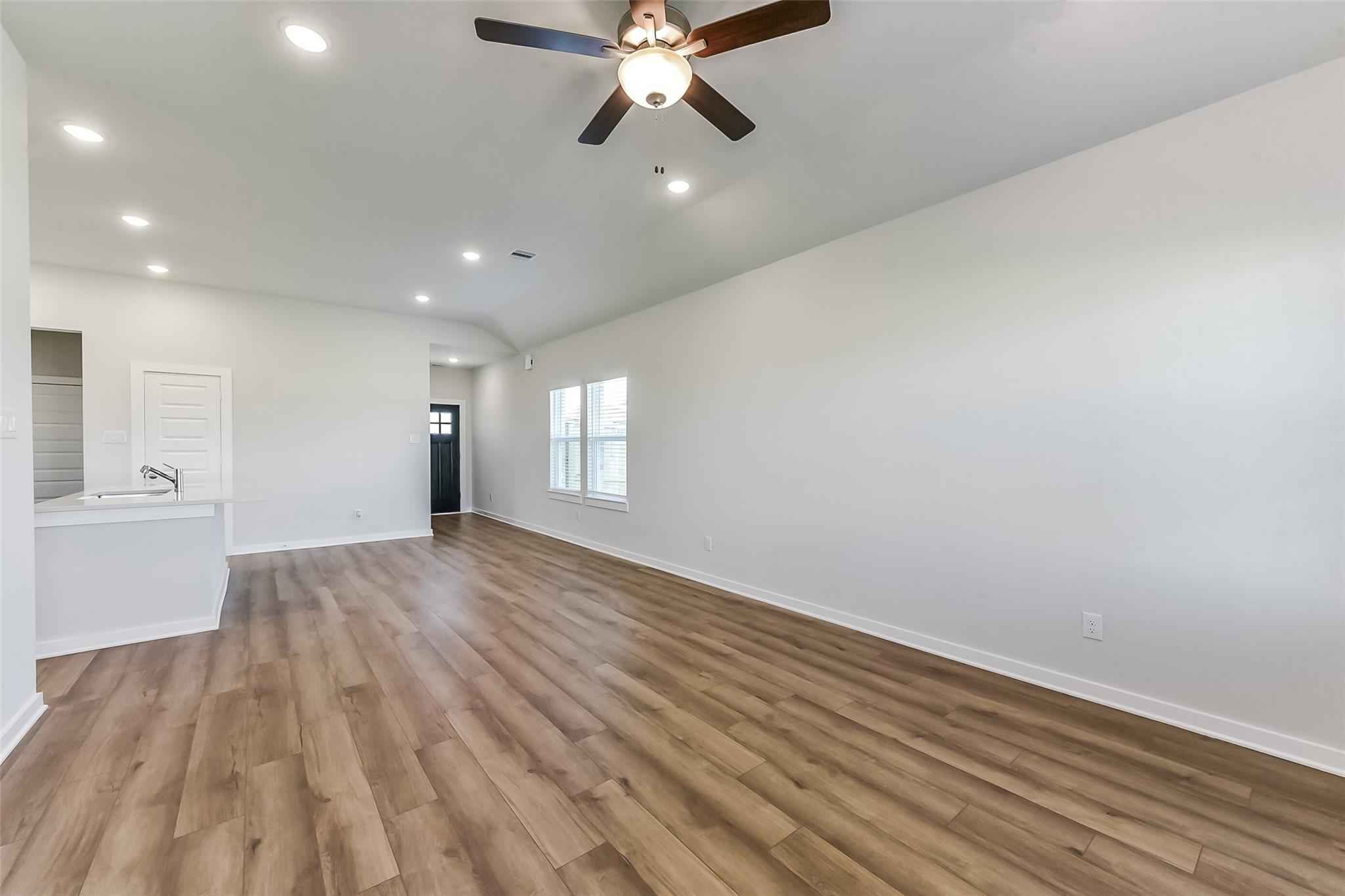 Spacious open living area with ceiling fan, recessed lights, laminate wood flooring, and kitchen sink bar in Davidson Homes The Costa C, Dayton Texas