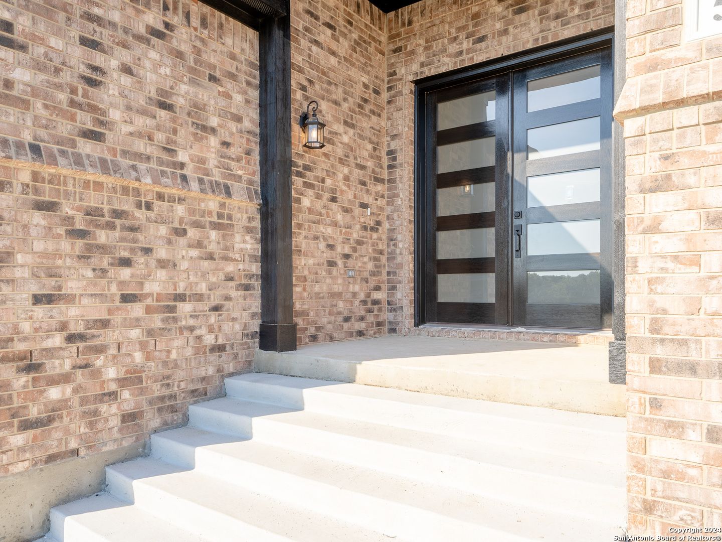 Modern frosted glass entry door with brick facade and hanging lantern in Davidson Homes The Summerlin A, Castroville, Texas