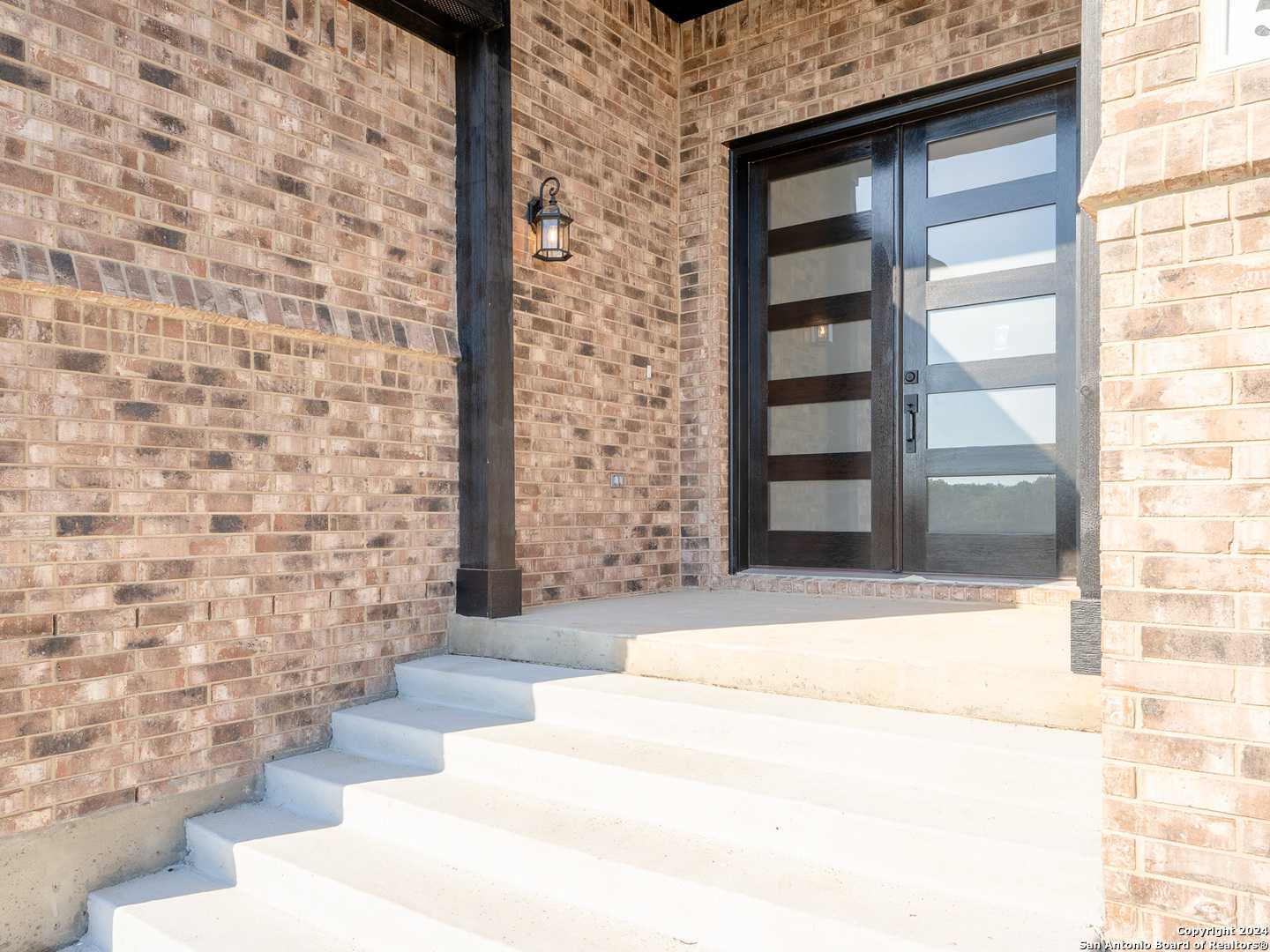 Modern frosted glass entry door with brick facade and hanging lantern in Davidson Homes The Summerlin A, Castroville, Texas