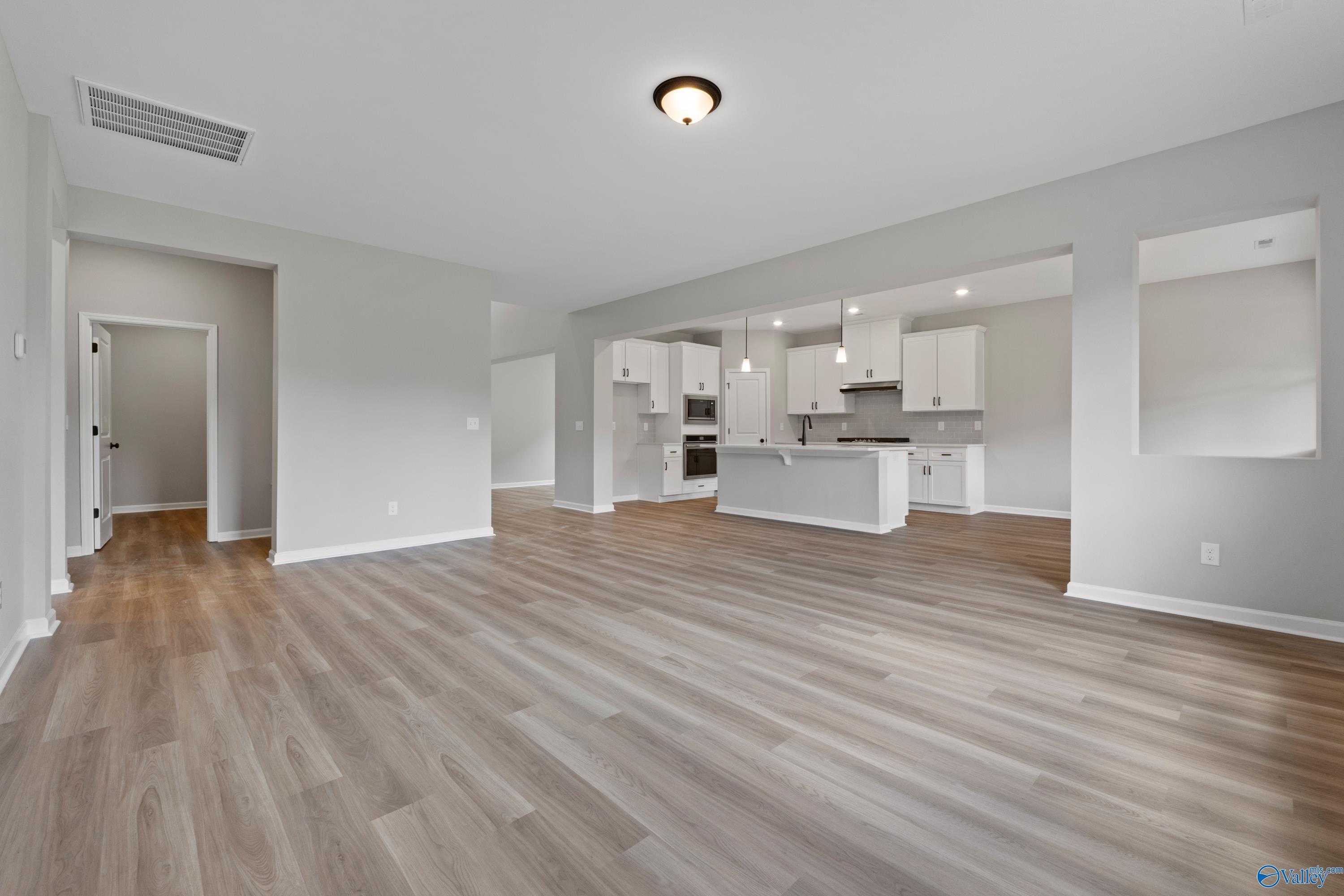 Open-concept living and kitchen with gray walls, white cabinets, island, and wood floors in Davidson Homes The Dorado, Huntsville, AL