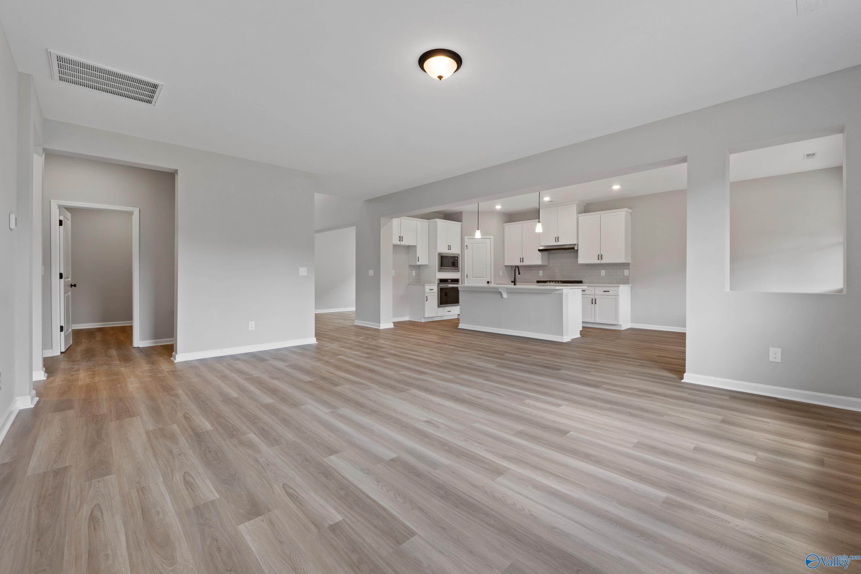 Open-concept living and kitchen with gray walls, white cabinets, island, and wood floors in Davidson Homes The Dorado, Huntsville, AL
