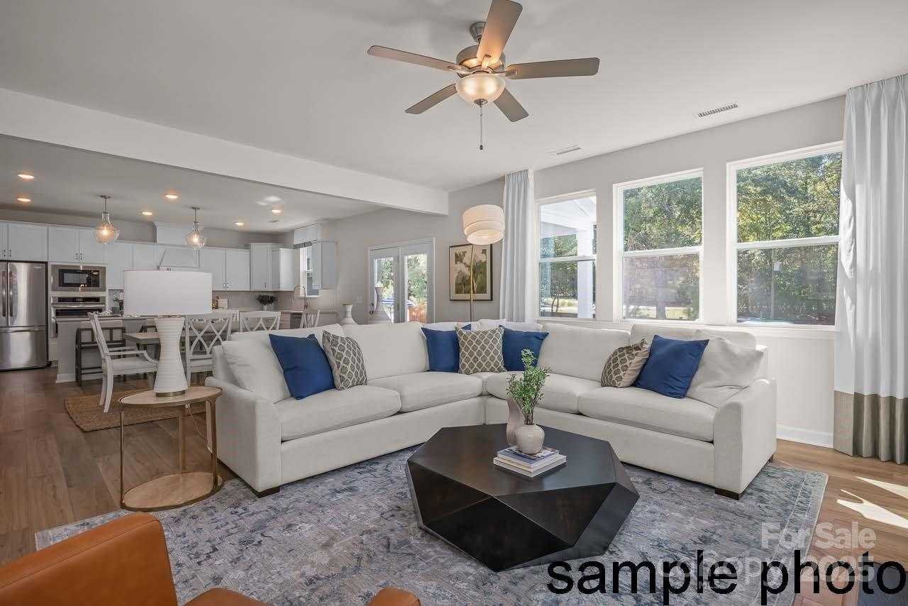 Open-concept living room with white L-shaped sofa, blue accents, geometric coffee table, and kitchen views in Davidson Homes The Hickory E II, Belmont, NC