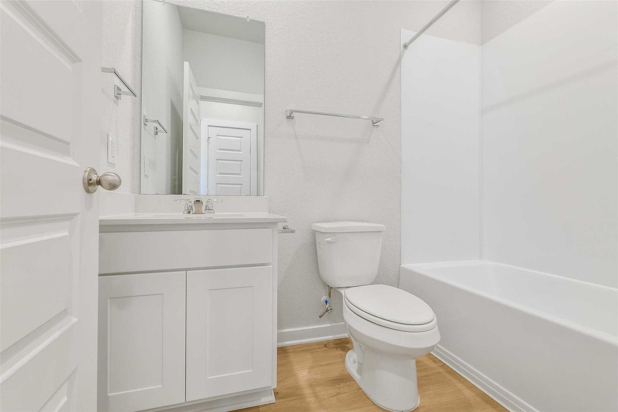 Bright white secondary bathroom with tub-shower combo, single vanity, and oak floors in Davidson Homes San Marcos E, Cleveland TX