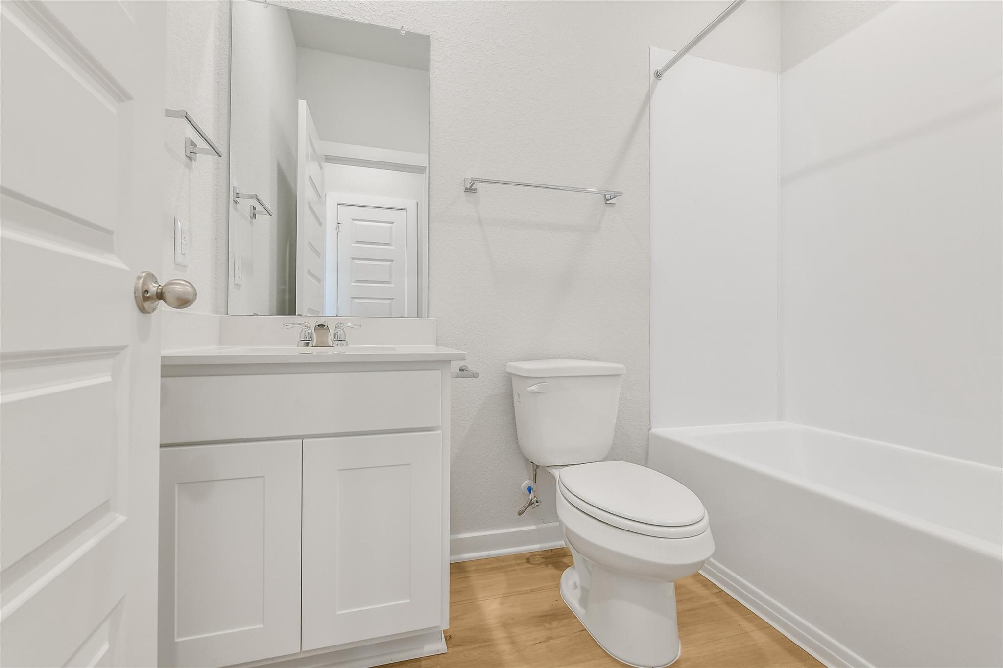 Bright white secondary bathroom with tub-shower combo, single vanity, and oak floors in Davidson Homes San Marcos E, Cleveland TX