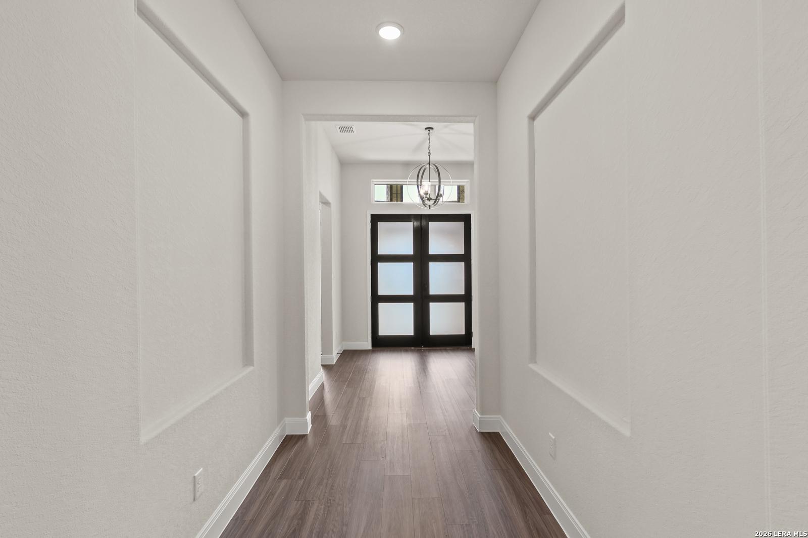 Elegant foyer with wood-look flooring and modern double front doors in The Summerlin B home at Potranco Oaks, Castroville.