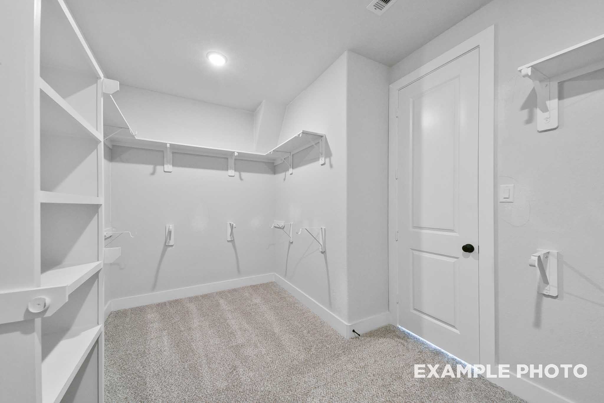 Spacious walk-in closet with white built-in shelves and hanging rods in Davidson Homes The George A, Lago Mar, Texas City