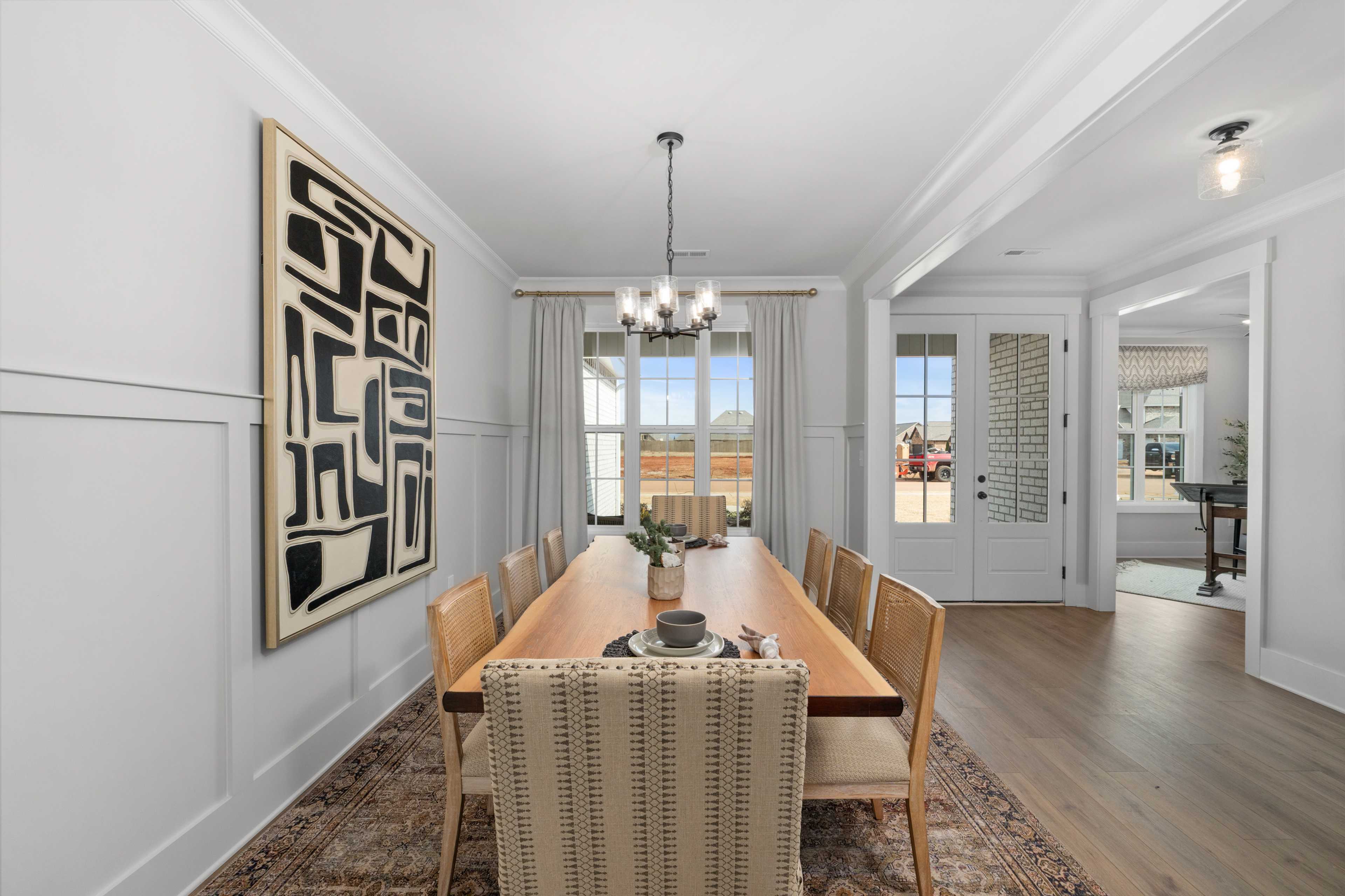 Spacious dining room in Briercreek Meridianville AL with long wooden table, upholstered chairs, abstract black art, chandelier, and large windows