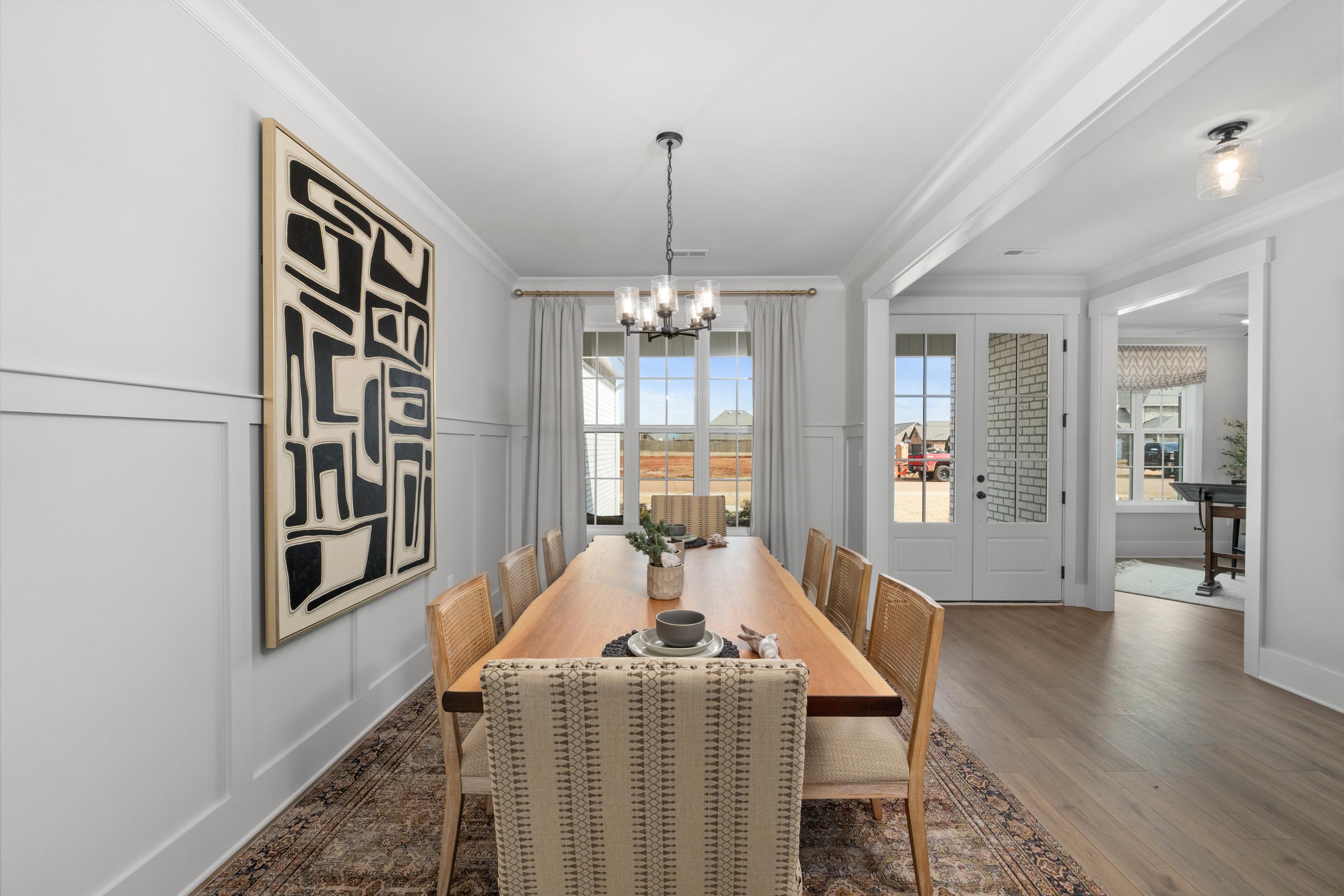 Spacious dining room in Briercreek Meridianville AL with long wooden table, upholstered chairs, abstract black art, chandelier, and large windows