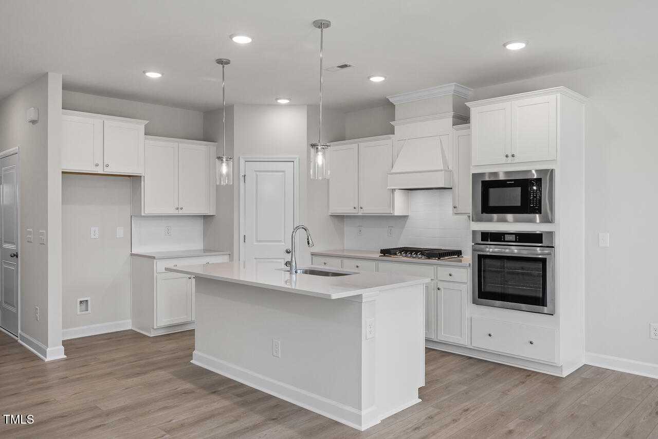Bright modern kitchen with white shaker cabinets, large island sink, stainless double ovens in Davidson Homes The Warren, Fuquay-Varina, NC