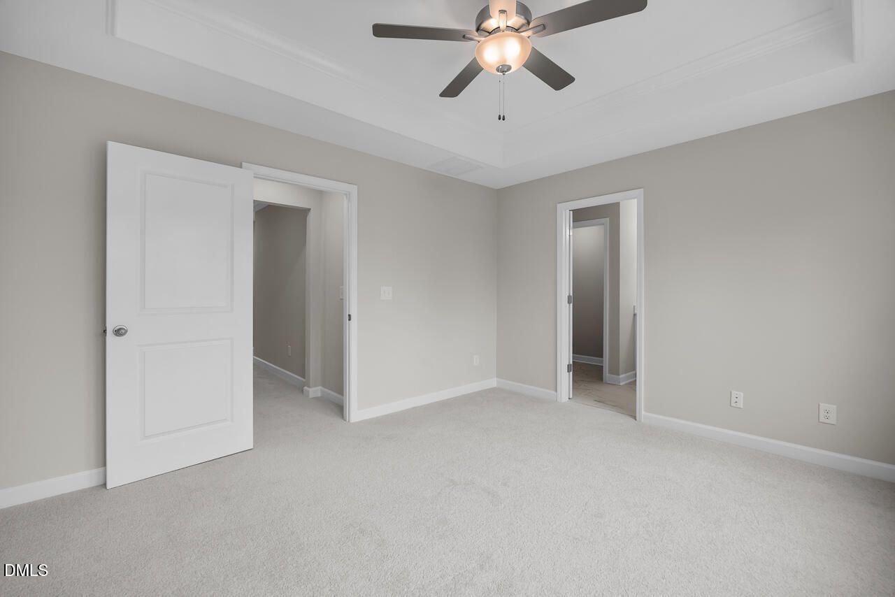 Spacious master bedroom with ceiling fan, light gray walls, plush carpet, open closet and bathroom doors in Davidson Homes The Avery, Knightdale NC