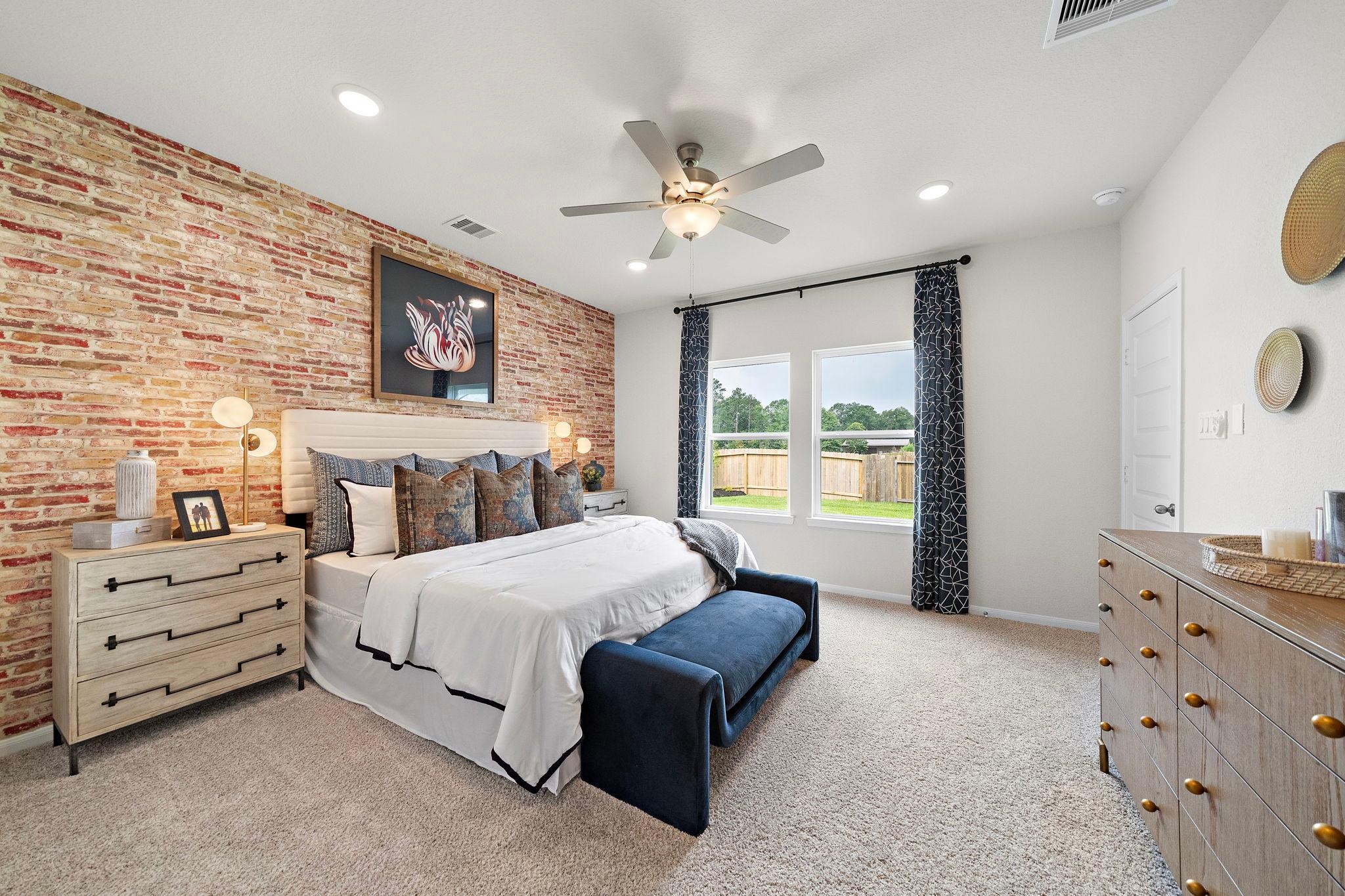 Spacious primary bedroom at Liberty Estates in Cleveland Texas with brick accent wall, king bed, and ceiling fan