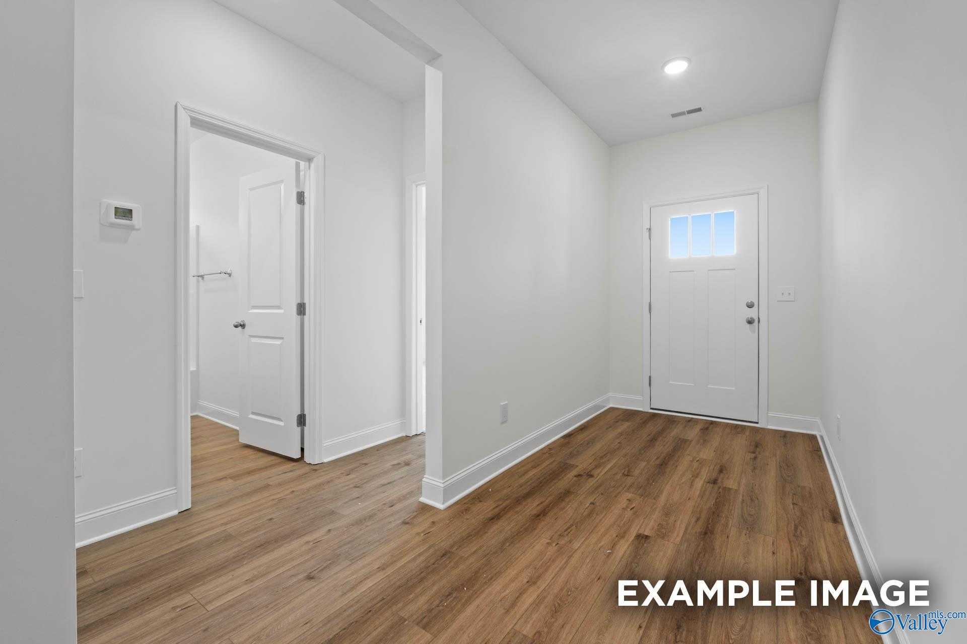 Bright entry hallway with hardwood floors, white doors, thermostat, and front entrance in Davidson Homes The Daphne D, Athens Alabama