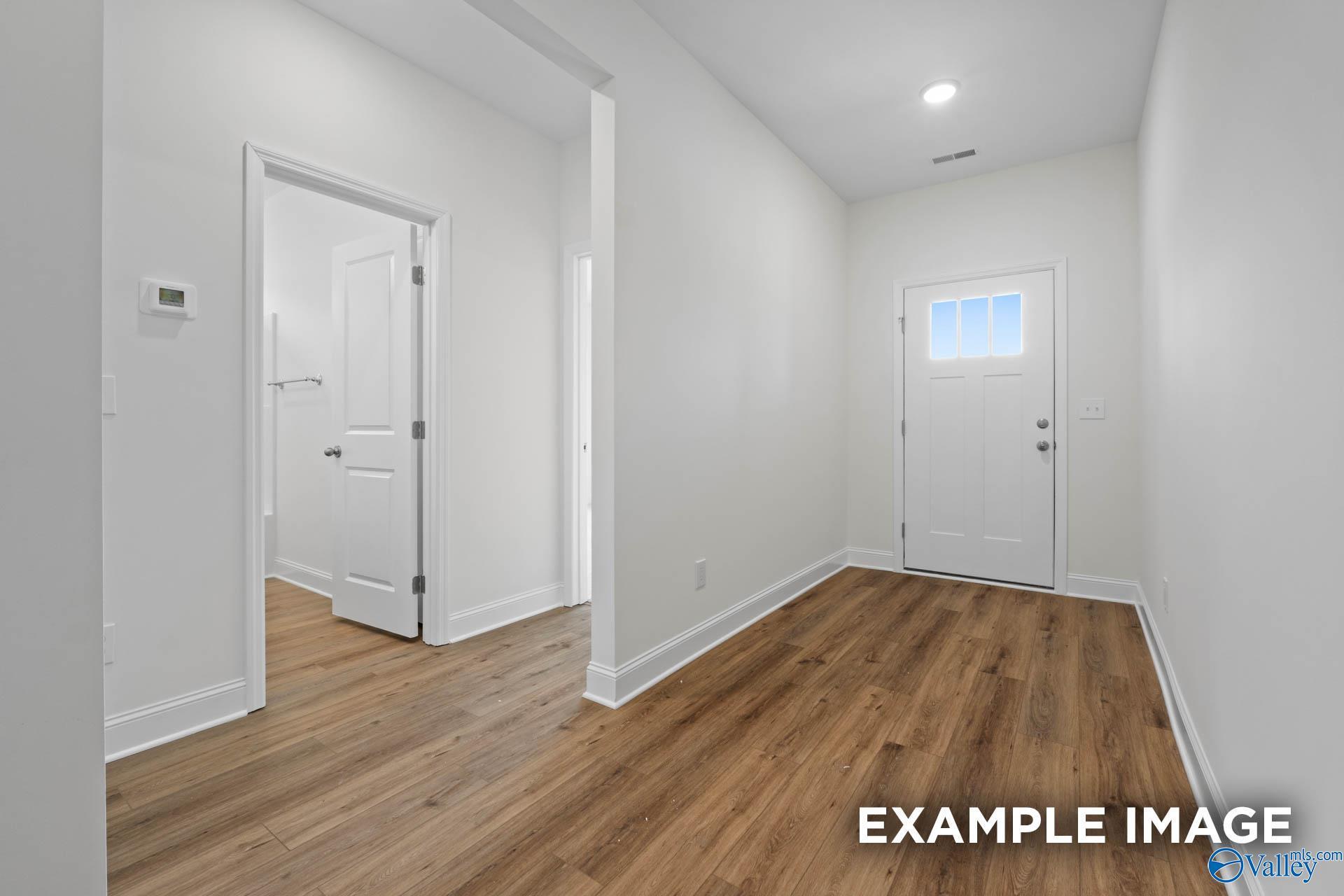 Bright hallway with white walls, hardwood floors, and front entry door in The Daphne E 4-bedroom home, Harvest, Alabama
