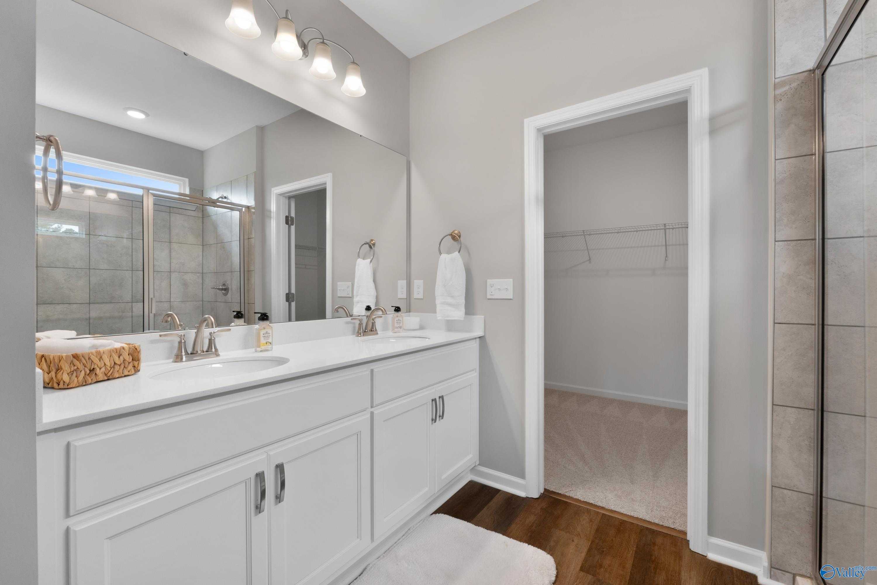 Modern master bathroom featuring double vanity, frameless glass shower, and adjacent closet in Evermore Homes The Noble, Madison AL