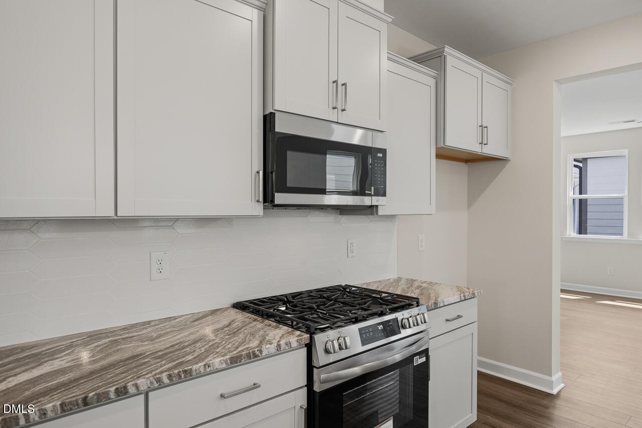 Modern kitchen with white cabinets, granite countertops, and stainless steel appliances in The Alexander C, Knightdale, NC.