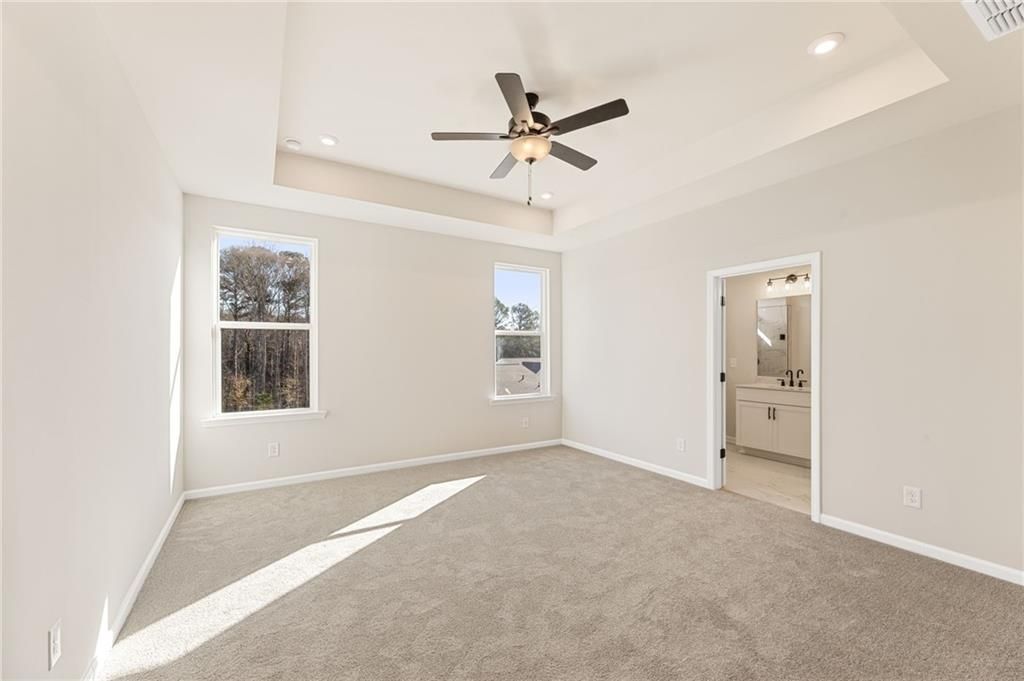 Bright bedroom featuring large windows, ceiling fan, and adjacent bathroom in Davidson Homes The Glenwood C, Loganville, GA