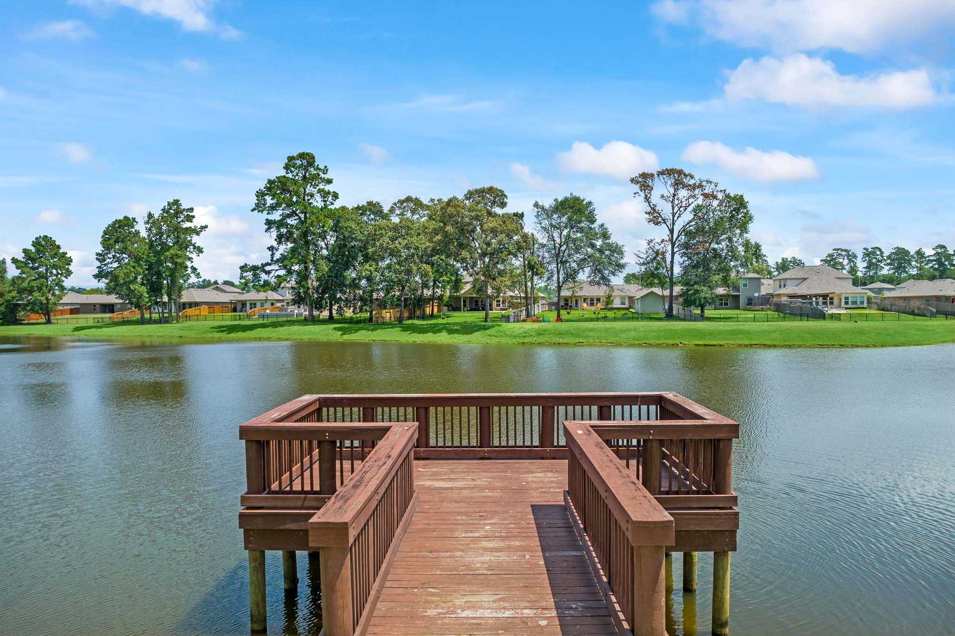 Serene wooden pier over lake at Lakes at Black Oak in Magnolia Texas with pine trees and homes