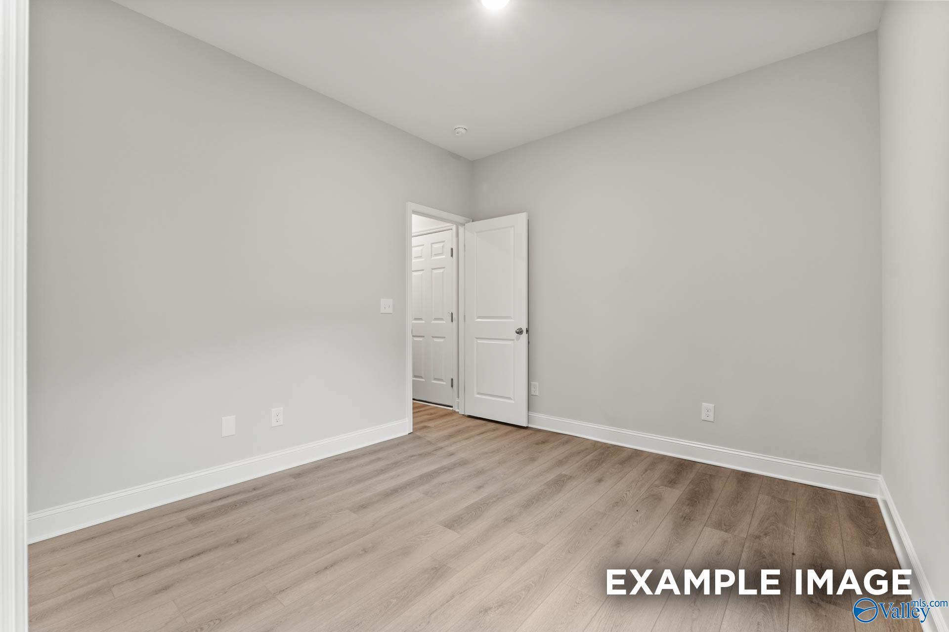 Spacious master bedroom with gray walls, open bath door, and hardwood floors in The Daphne 4-bedroom home, Meridianville, Alabama