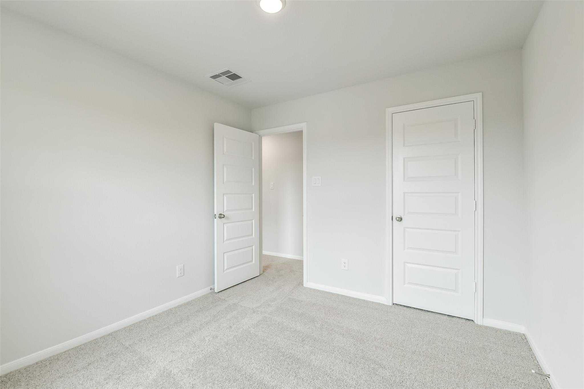 Bright secondary bedroom with light gray walls, white doors, and beige carpet in Davidson Homes The Brazos F, Conroe, Texas