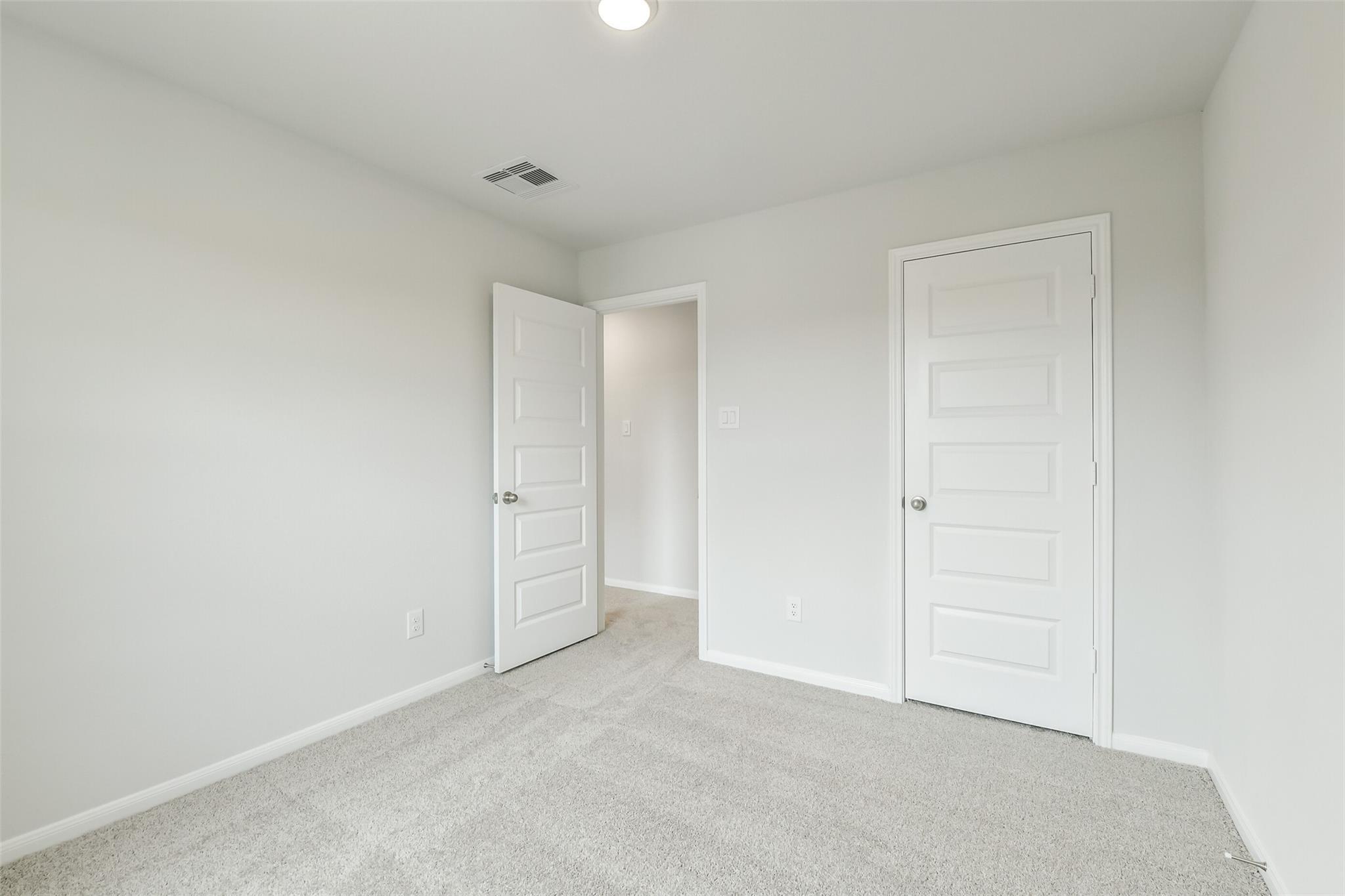 Bright secondary bedroom with white walls, gray carpet, open closet door in 5-bedroom Davidson Homes The Brazos F, Conroe Texas