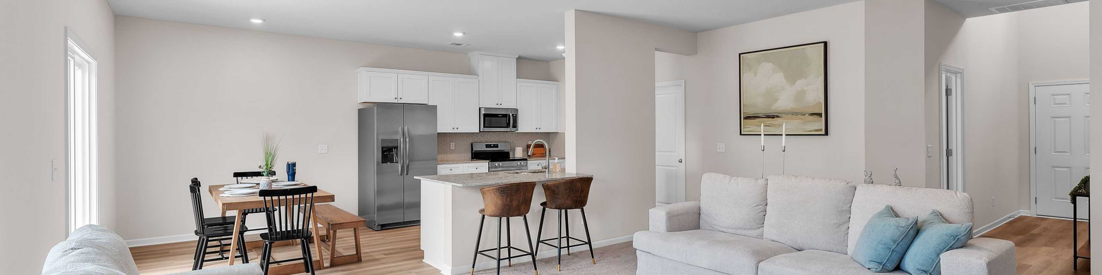 Spacious open-concept living room and kitchen at Summer Vineyard in Phenix City AL with white sofas, island bar, and stainless appliances