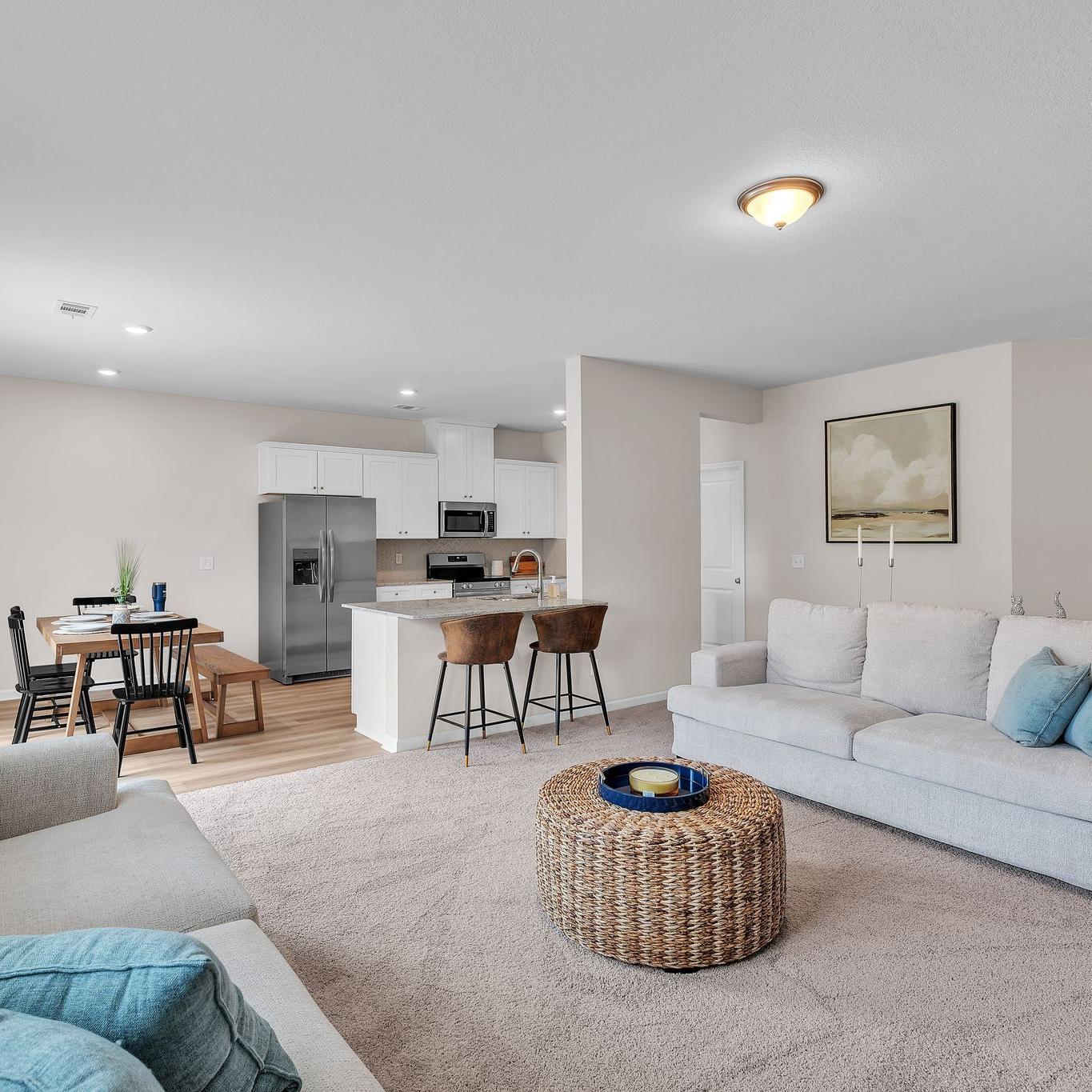 Spacious open-concept living room and kitchen at Summer Vineyard in Phenix City AL with white sofas, island bar, and stainless appliances