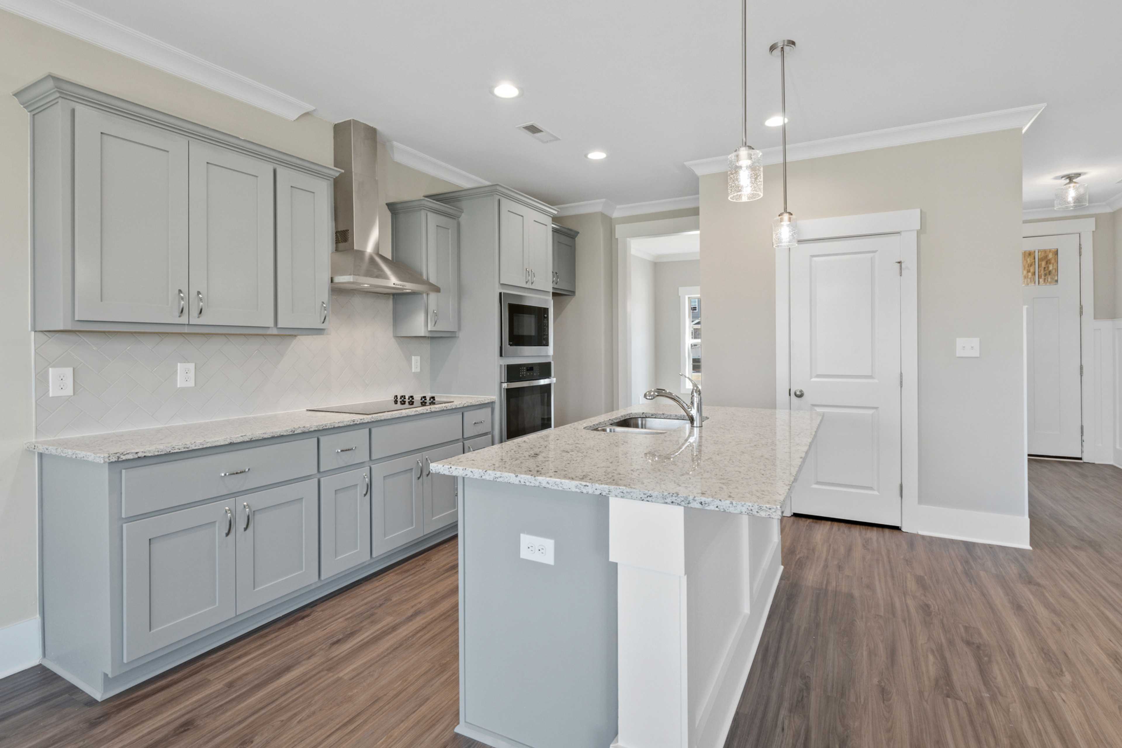 Spacious modern kitchen with gray shaker cabinets, granite island, and hardwood floors at Little Burwell Estates in Harvest, Alabama