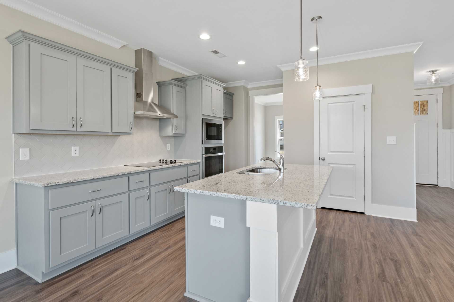 Spacious modern kitchen with gray shaker cabinets, granite island, and hardwood floors at Little Burwell Estates in Harvest, Alabama
