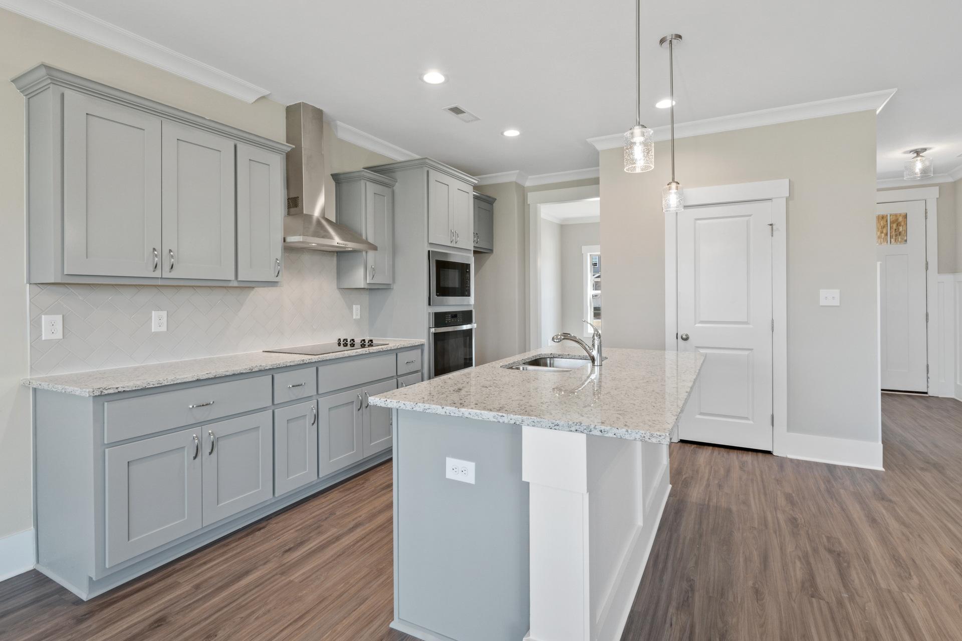 Spacious modern kitchen with gray shaker cabinets, granite island, and hardwood floors at Little Burwell Estates in Harvest, Alabama