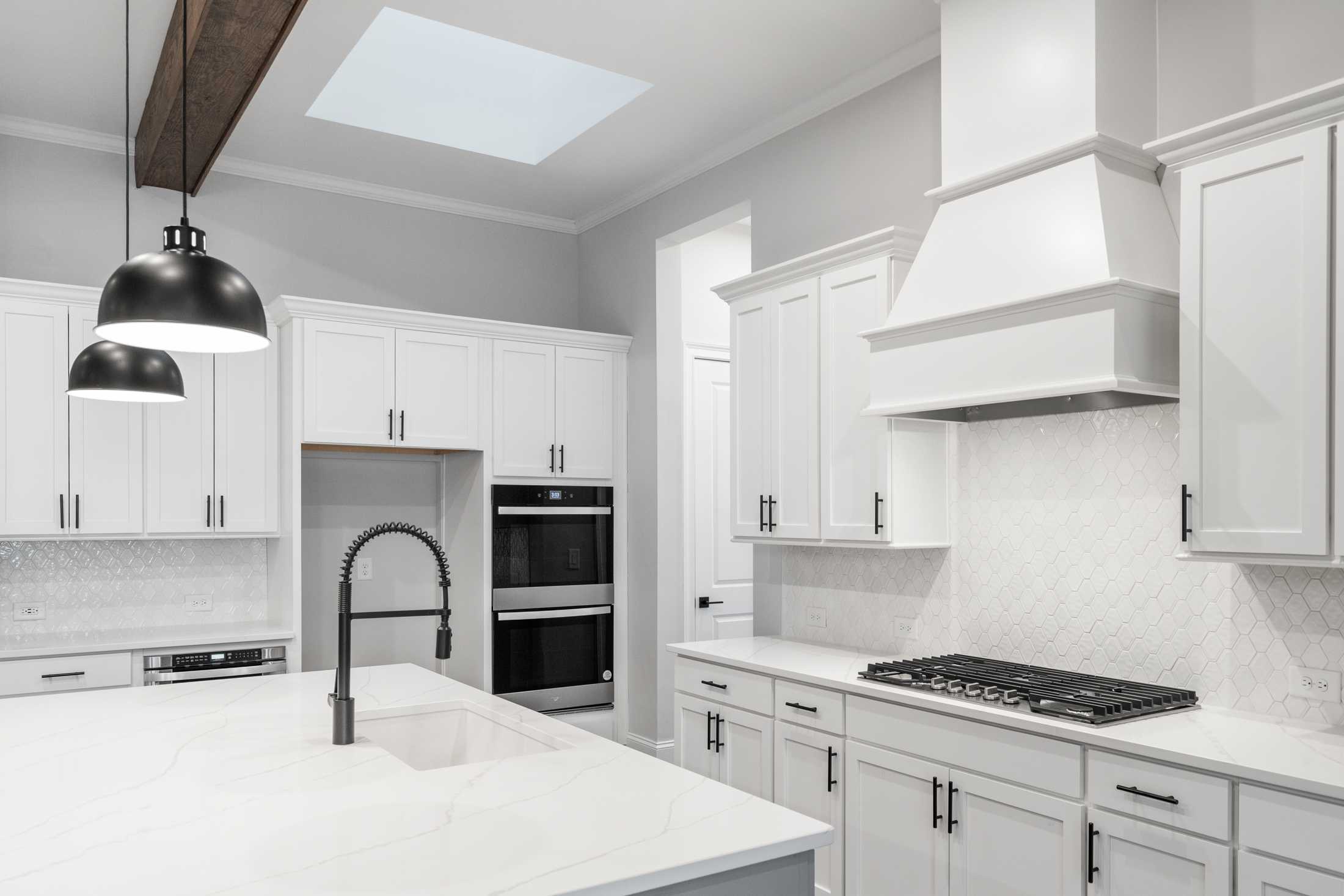 Modern white kitchen in The Seaside home with shaker cabinets, quartz island, gas range, subway tile backsplash, and skylight