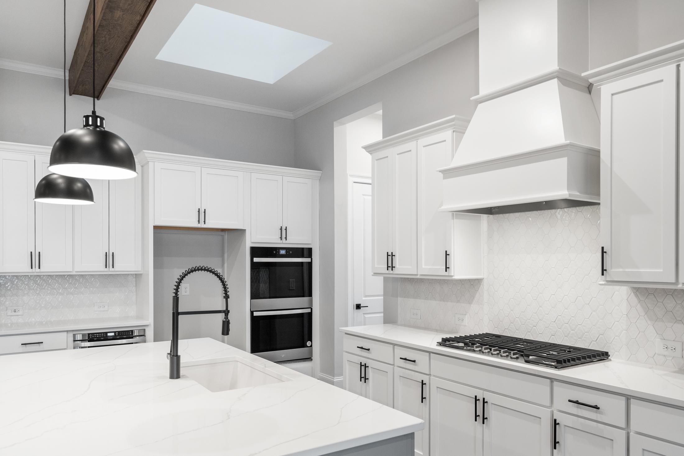 Modern white kitchen in The Seaside home with shaker cabinets, quartz island, gas range, subway tile backsplash, and skylight