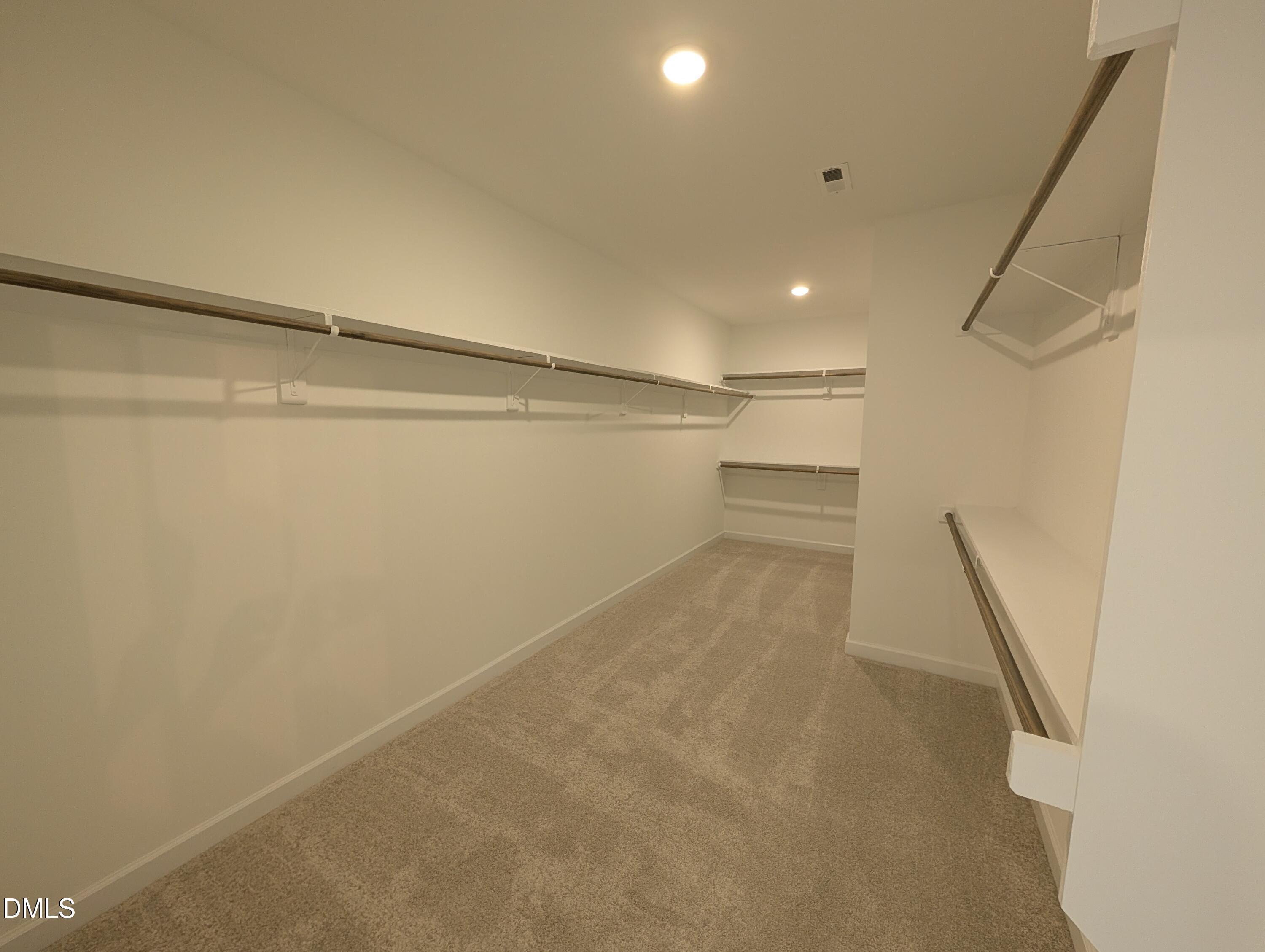 Spacious walk-in closet with carpet and built-in shelving in The Aspen B floor plan at Wendell Ridge, Wendell, NC.