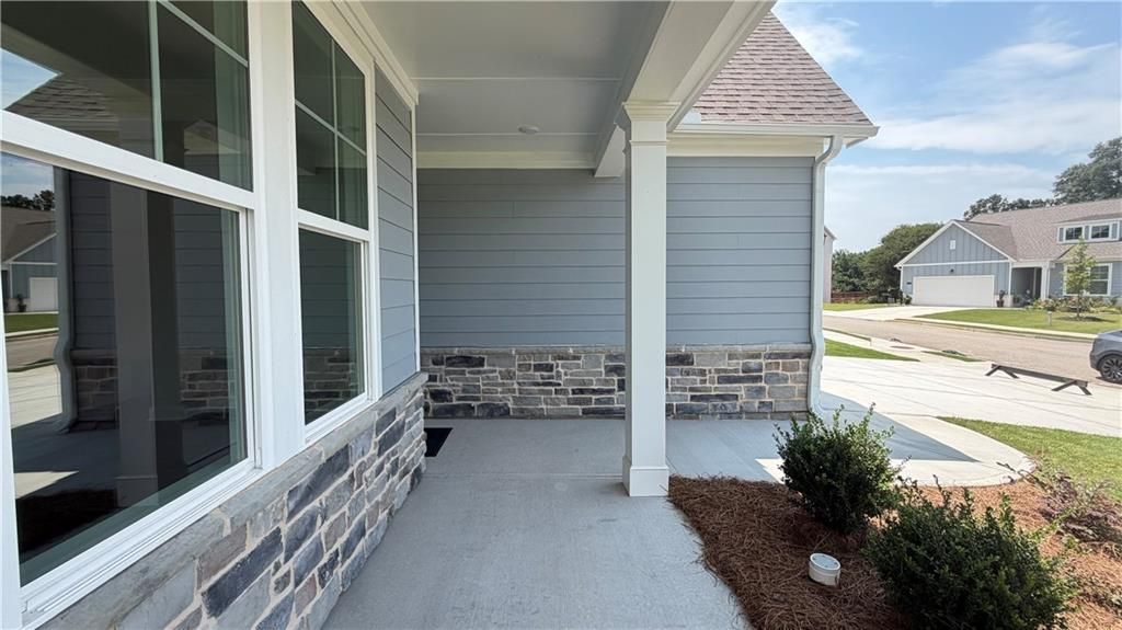 Covered front porch with stone accents and grey siding on The Ash C floor plan in Wehunt Meadows, Hoschton, Georgia.