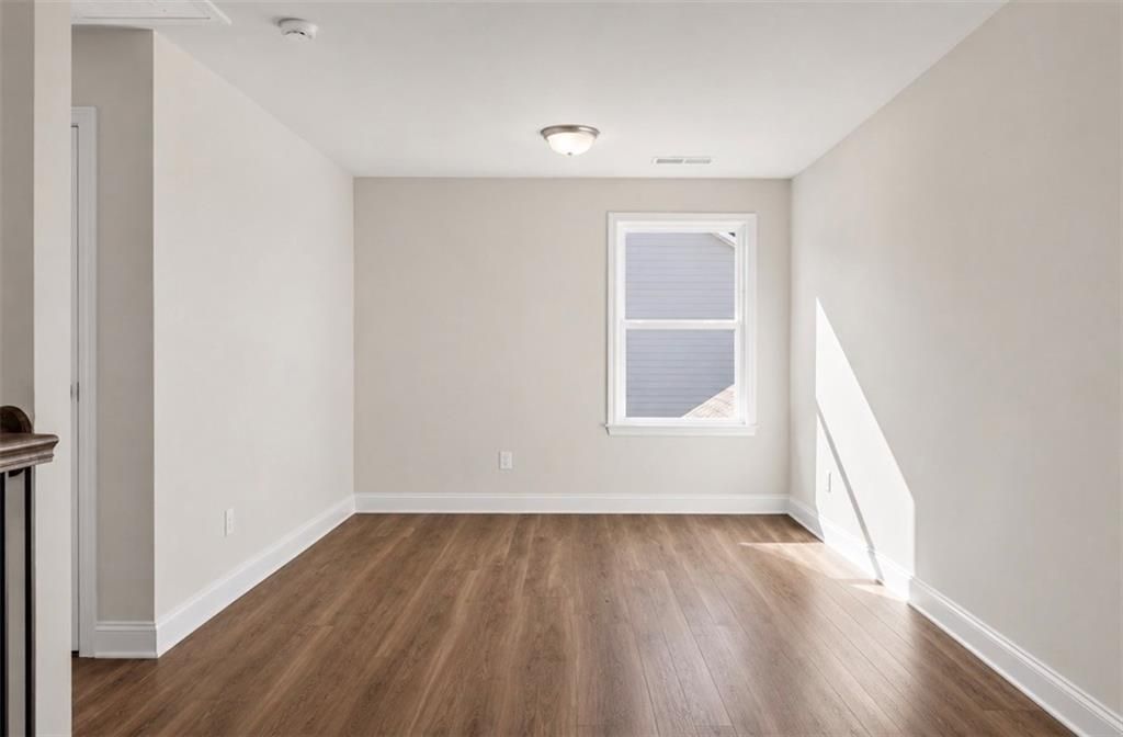 Bright, spacious secondary bedroom with wood-look flooring in The Ash C floor plan at Wehunt Meadows in Hoschton, Georgia.