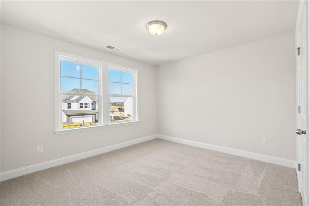 Bright secondary bedroom with beige carpet, light gray walls, and large windows overlooking neighborhood in Davidson Homes The Ash C, Hoschton