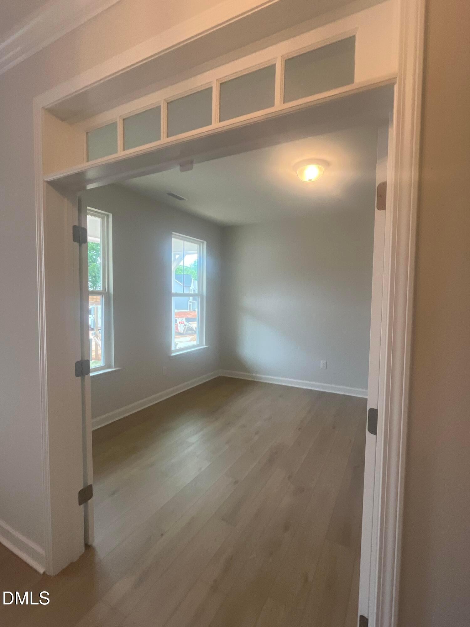 Bright empty bedroom with light gray walls, hardwood floors, large windows, and arched doorway in Davidson Homes The Birch II E, Wake Forest, NC