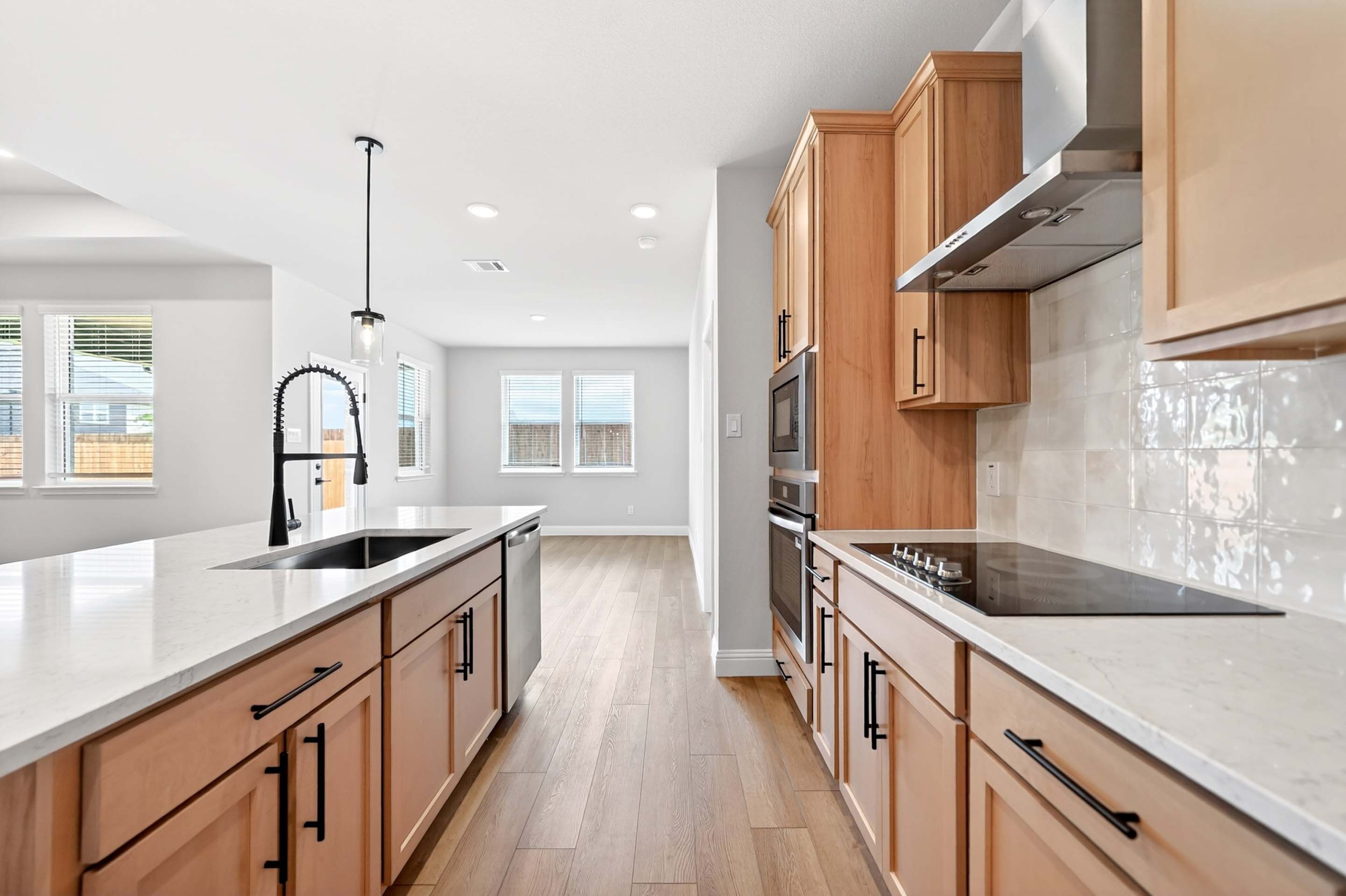 Modern kitchen in The Holly featuring a large island, light wood cabinets, quartz countertops, and stainless appliances.