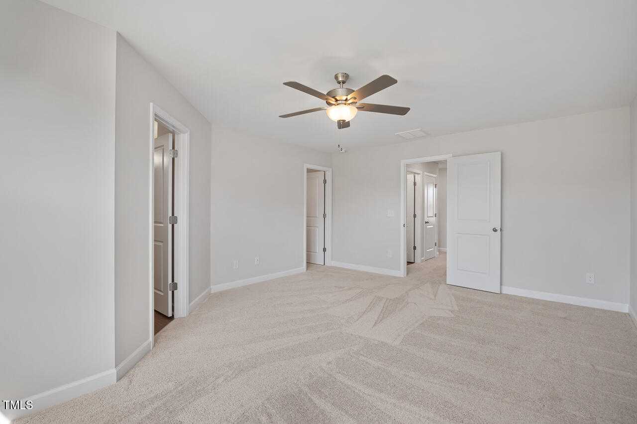 Spacious secondary bedroom with neutral walls, ceiling fan, and adjacent doors in Davidson Homes The Graham, Fuquay-Varina, NC