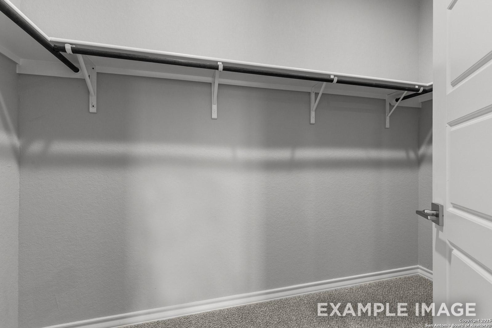 Spacious walk-in closet in The Oxford H master suite featuring wall-mounted shelving and hanging rods.