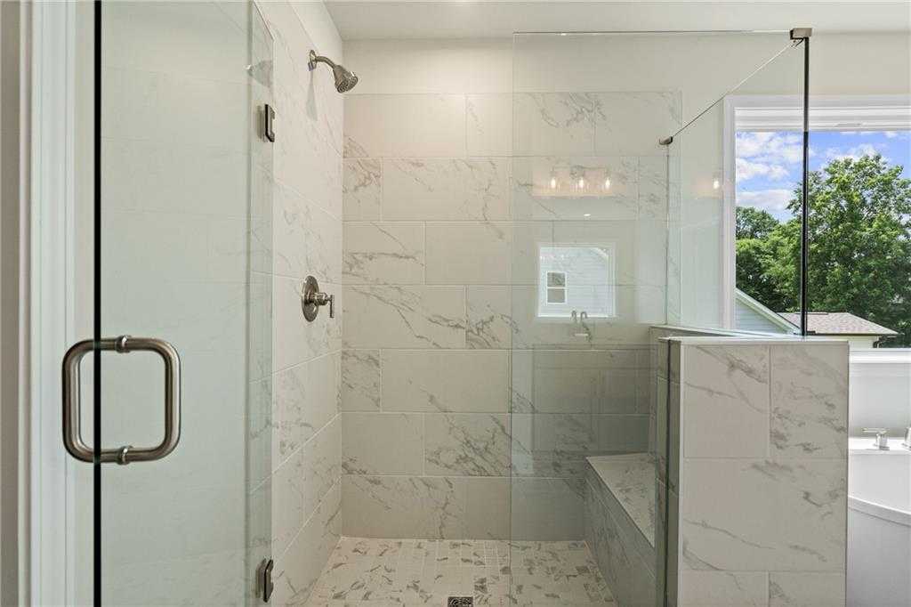 Elegant frameless glass shower with white marble tiles, built-in bench, and rain head in master bath of Davidson Homes The Hickory B in Hoschton, GA