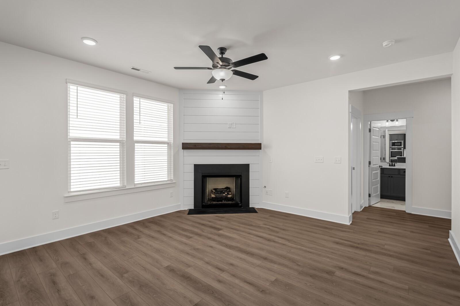 Living room with corner fireplace, shiplap detail, and wood-style floors in The Willow home at Woods Crossing, Gallatin.