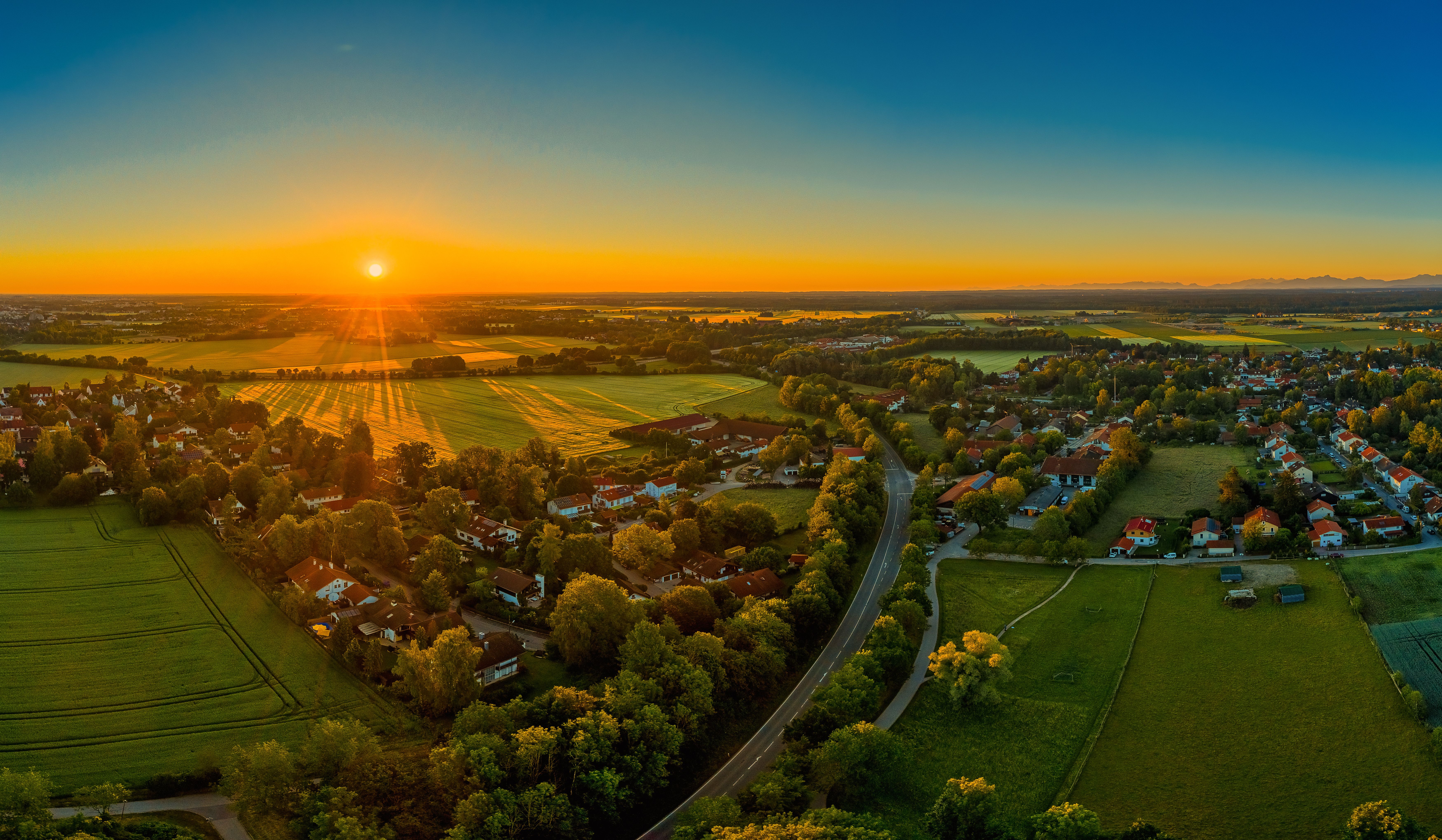 Sunset aerial view of new home community in Tanner amid golden fields, tree-lined roads, and villages