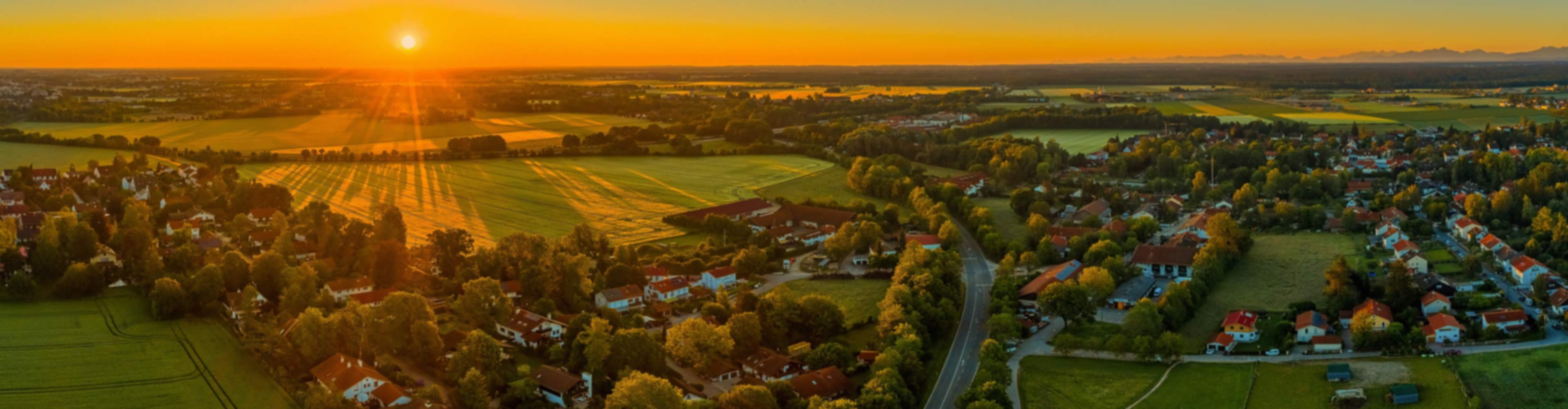 Sunset aerial view of new home community in Tanner amid golden fields, tree-lined roads, and villages