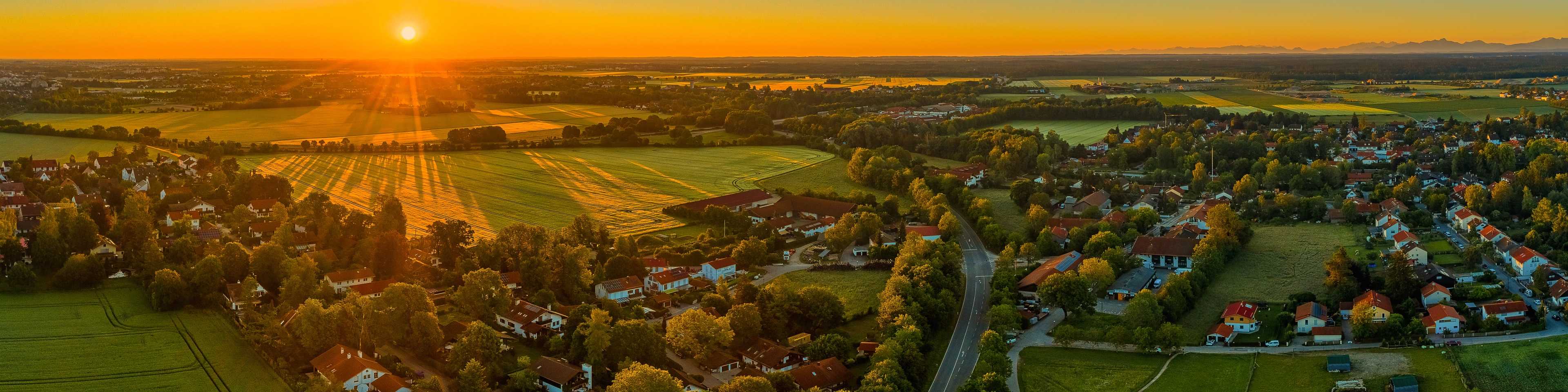 Sunset aerial view of new home community in Tanner amid golden fields, tree-lined roads, and villages