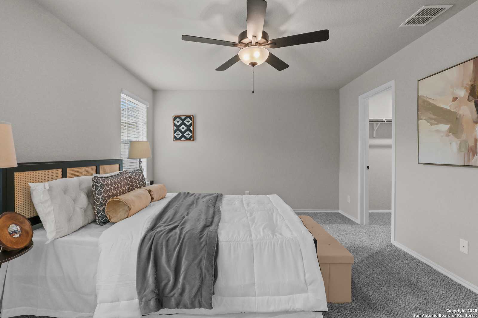 Cozy master bedroom with king bed, ceiling fan, lamps, and walk-in closet in Davidson Homes The Charlotte B, San Antonio